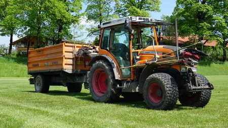 Orangener Bauhof Traktor mit Anhänger. 